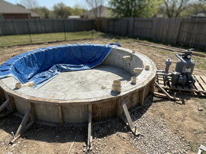 Runder Gartenpool im Bau: Betonkern, Holzform, blaue Vinyl-Liner, Filterpumpe, Einlässe, Tageslicht.
